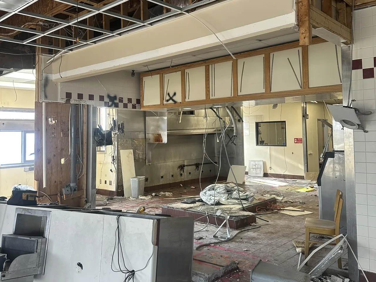 The Al Manakeesh space in Fishers mid-demolition: ceiling grid and wood framing exposed, the kitchen line stripped to bare stainless, and debris across the floor.