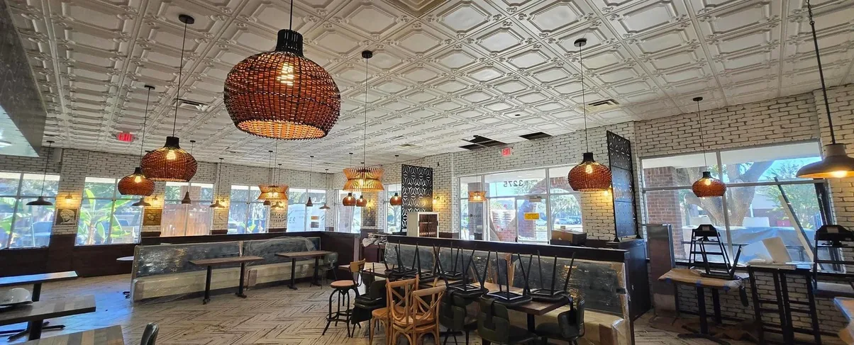 The Da Vinci Restaurant dining room: a pressed-tin ceiling, woven rattan pendants, and banquette seating running along an exposed brick wall.
