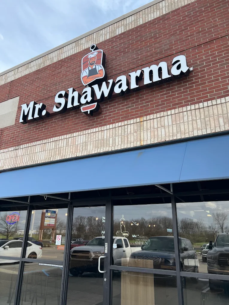 The finished Mr. Shawarma storefront: illuminated channel-letter signage and logo mounted on brick above a blue awning and a full-height glass entry.