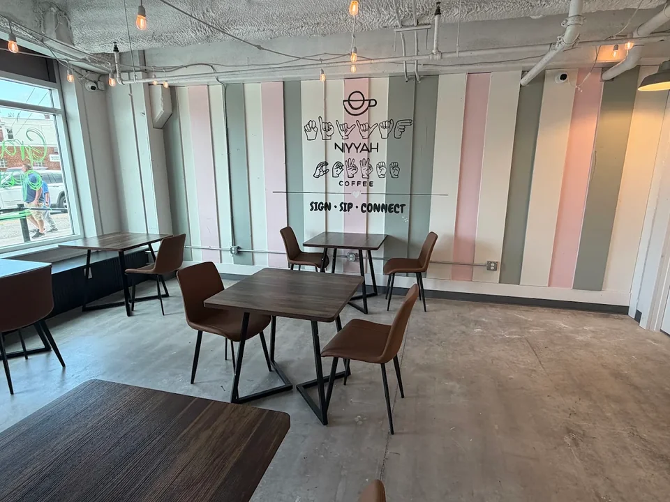 The finished Niyyah Coffee dining room: a pink and sage striped feature wall carrying the Niyyah wordmark behind walnut two-tops on polished concrete.